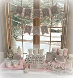 a pink table topped with lots of cupcakes and desserts next to a window