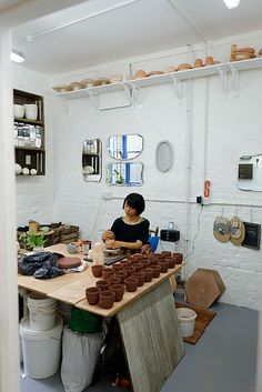 a woman sitting at a table with lots of clay pots on it's sides