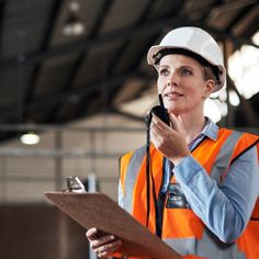 a woman in an orange safety vest holding a clipboard and looking up at something