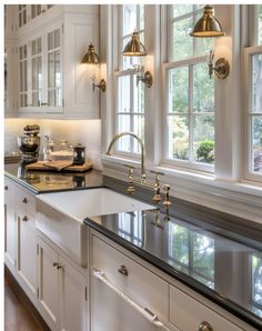 a kitchen with white cabinets and black counter tops, gold faucets and brass fixtures