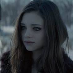 a woman with long brown hair and blue eyes staring at the camera, in a snowy area