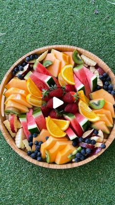 a wooden bowl filled with fruit on top of a green grass covered field next to a white dog