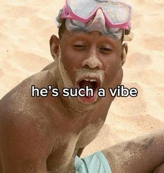 a man with goggles on his head sitting in the sand and making a funny face