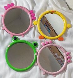 three colorful mirrors sitting on top of a white bed next to each other, one with pink and green flowers