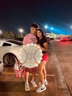 two people standing next to each other holding up a sign that says light up the world with baseballs on it