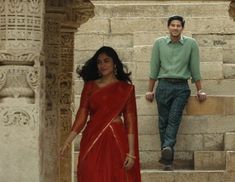 a woman in a red sari walking up some steps next to a man wearing a green shirt