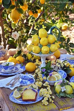 a table with lemons, bread and flowers on it in front of a tree