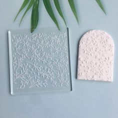 two ceramic tiles sitting on top of a table next to green leafy plant leaves