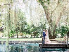 a bride and groom standing on a bridge over water