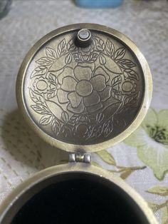 an antique looking pocket watch sitting on top of a floral print tablecloth with flowers