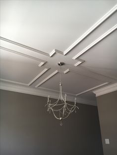 a chandelier hanging from the ceiling in a room with gray walls and white trim