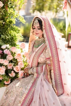 a woman in a white and pink bridal outfit sitting on a bench with flowers