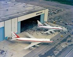 two airplanes are parked in front of an airplane hangar with people walking around it and cars on the ground