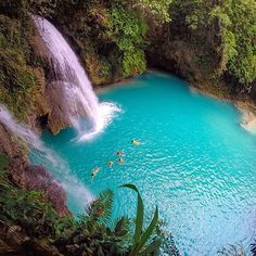 people are swimming in the blue water near a waterfall and some green trees on either side