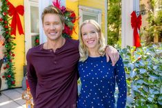 a man standing next to a woman in front of a yellow house with christmas decorations