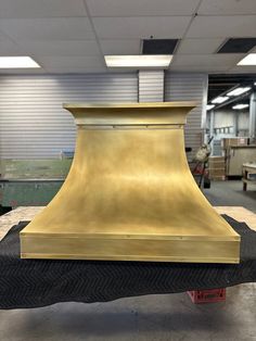 a gold colored stove hood sitting on top of a piece of black material in a shop