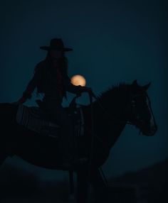 a woman riding on the back of a black horse at night with a full moon in the background