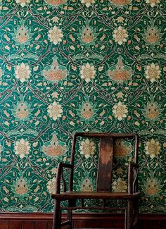 an old wooden chair sitting in front of a green wallpapered room with wood flooring