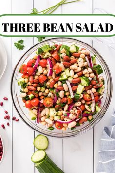 a salad with beans, cucumbers and red onions in a glass bowl on a white table