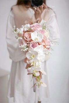 a woman holding a bouquet of pink and white flowers in front of her wedding dress