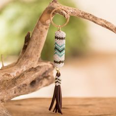 a beaded keychain hanging from a tree branch with beads and tassels