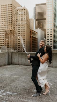 a man and woman are dancing in an open area with tall buildings behind them while holding each other's hands