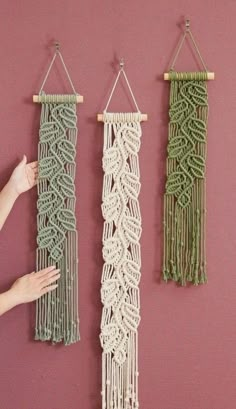 two macrame wall hangings are hung on a pink wall, one is green and the other is white