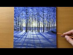 someone is painting a snowy forest scene with blue and yellow colors on the wood table