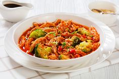 a white bowl filled with noodles and broccoli next to a cup of coffee