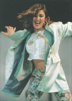 a woman in white shirt and floral pants with jacket on her shoulders, arms outstretched