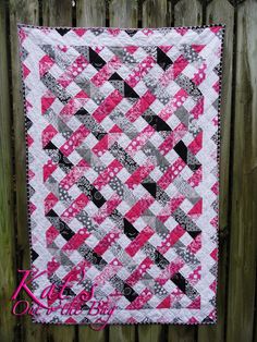 a pink and black quilt hanging on a fence