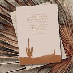 a wedding card with a desert scene and palm leaves on the ground next to it