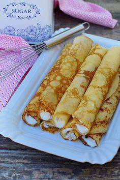 three crepes on a white plate next to a cup and whisk