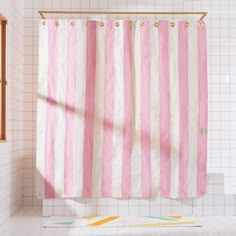 a pink and white striped shower curtain in a bathroom with tile flooring next to a window