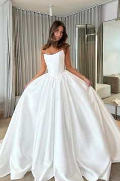 a woman wearing a white wedding dress in front of a mirror with her hands on her hips