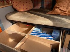 an open box sitting on top of a wooden bench next to a pillow and pillows