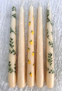 four candles with flowers painted on them sitting next to each other in front of a white towel