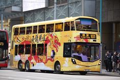 two double decker buses are parked on the side of the street as people stand near by