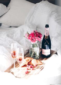 there is a bottle of wine and two glasses on the bed with flowers in it