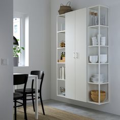 a white cabinet with glass doors and shelves in the corner next to a dining room table