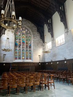 an empty church with wooden chairs and chandelier hanging from the ceiling in front of stained glass windows