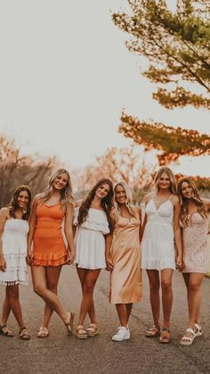 the bridesmaids are all dressed in white and orange dresses, posing for a photo