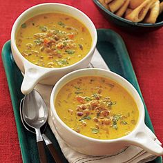 two bowls of soup on a tray with silver spoons