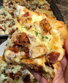 someone holding up a piece of pizza with bacon and cheese on it, in front of other slices