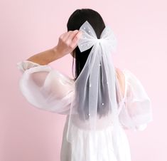 a woman in a white dress is wearing a veil and holding her hair back to the camera