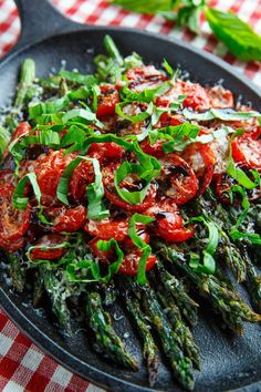 asparagus and tomatoes in a skillet on a checkered tablecloth