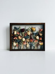 a wooden frame with flowers in it sitting on a table next to a white wall