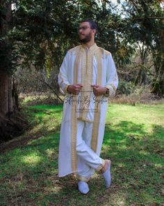 a man standing in the grass with his hands on his hips wearing white and gold clothing