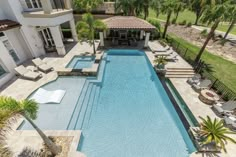 an aerial view of a swimming pool with lounge chairs and palm trees in the background