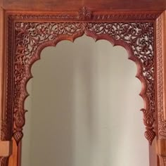 an ornate wooden mirror frame with carvings on the top and bottom edge, in front of a white wall